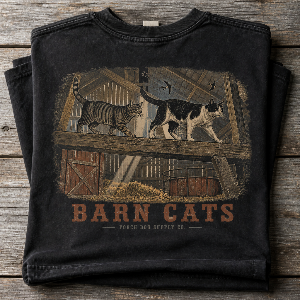 Barn Cats vintage-washed black tee folded on weathered barnwood, back art of cats walking the hayloft rafters