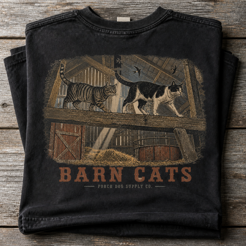 Barn Cats vintage-washed black tee folded on weathered barnwood, back art of cats walking the hayloft rafters