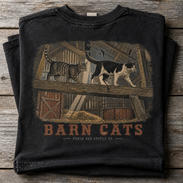 Barn Cats vintage-washed black tee folded on weathered barnwood, back art of cats walking the hayloft rafters