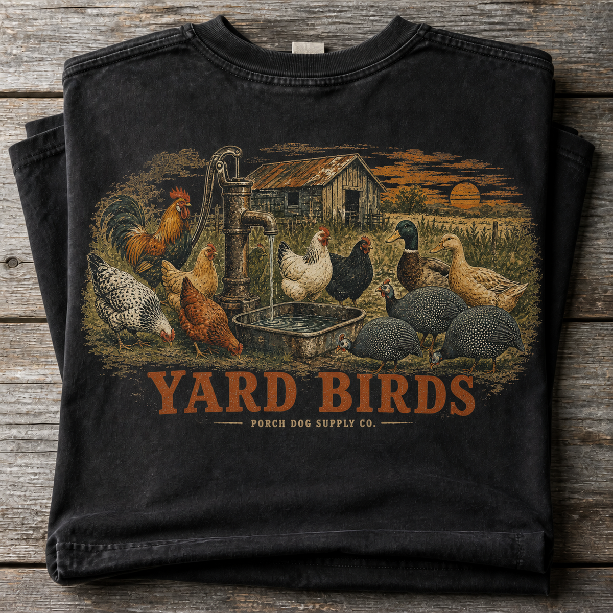 Yard Birds vintage-washed black tee folded on weathered barnwood, back art of chickens and guineas at the water pump